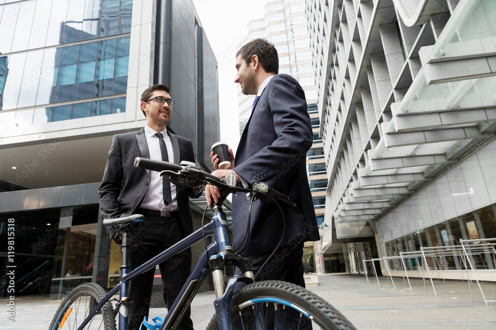 Two young businessmen with a bike in city centre Two young businessmen with a bike in city centre