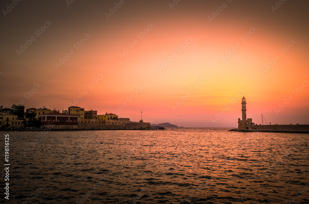 The old lighthouse of Chania at sunset, Crete Island, Greece. View of the old venetian port of Chania on Crete island Greece. Tourists relaxing on promenade.