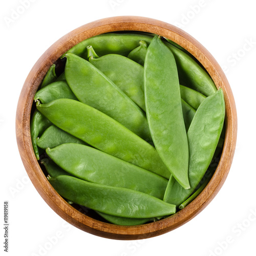 Snow peas in a wooden bowl on white background. Pisum sativum saccharatum, a green legume and variety of pea, eaten whole in its pod while still unripe. Isolated macro food photo close up from above.