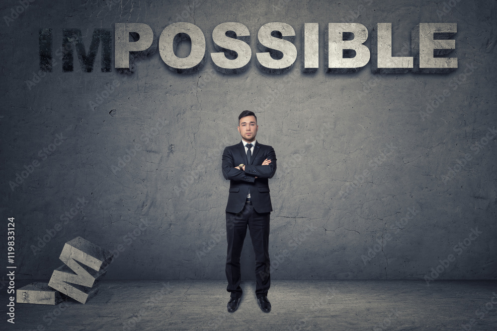 Obraz premium Front view of a buisnessman standing with folded arms under big 3d concrete word 'possible'