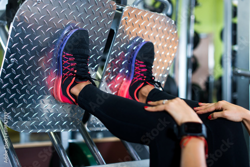 Close up shoes of a fit young woman doing leg press in the gym photo