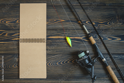 Fototapeta Naklejka Na Ścianę i Meble -  Fishing tackle with a bait for a predator on a wooden dark background a table and a notebook with the place for the text