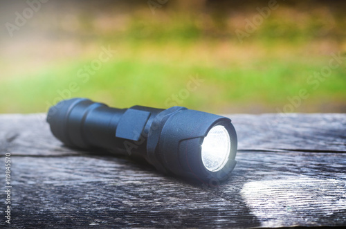 Tactical waterproof flashlight on wooden base with light beam