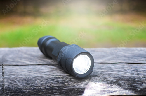 Tactical waterproof flashlight on wooden base with light beam