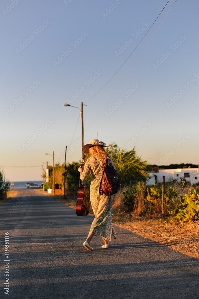 Obraz premium Stylish hipster woman on blue sky countryside remote road outdoors background