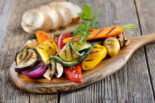 Vegan grillen: Gemischtes Gemüse vom Grill mit Kräutern, Gewürzen und Olivenöl, dazu frisches Ciabattabrot - Mixed grilled vegetables on a wooden cutting board served with Italian ciabatta bread