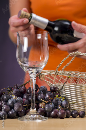 Fototapeta Naklejka Na Ścianę i Meble -  Woman opening a bottle of red wine, behind a glass stemware and cluster of red grapes