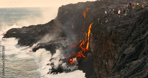 Tourist looking at Volcanic Eruption Lava flowing into the ocean. Steam rising from waves as molten lava flows into ocean waters Big Island Hawaii.