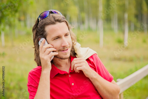 Young man walking in the park in summer and he speaking on the mobile phone.