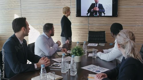 Business team sitting in the meeting room and listening to their boss speaking from TV screen while video conference photo