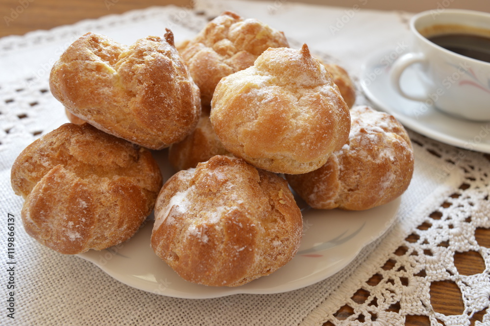 Delicious, small homemade cream puffs powdered with icing sugar on white plate and cup of coffee

