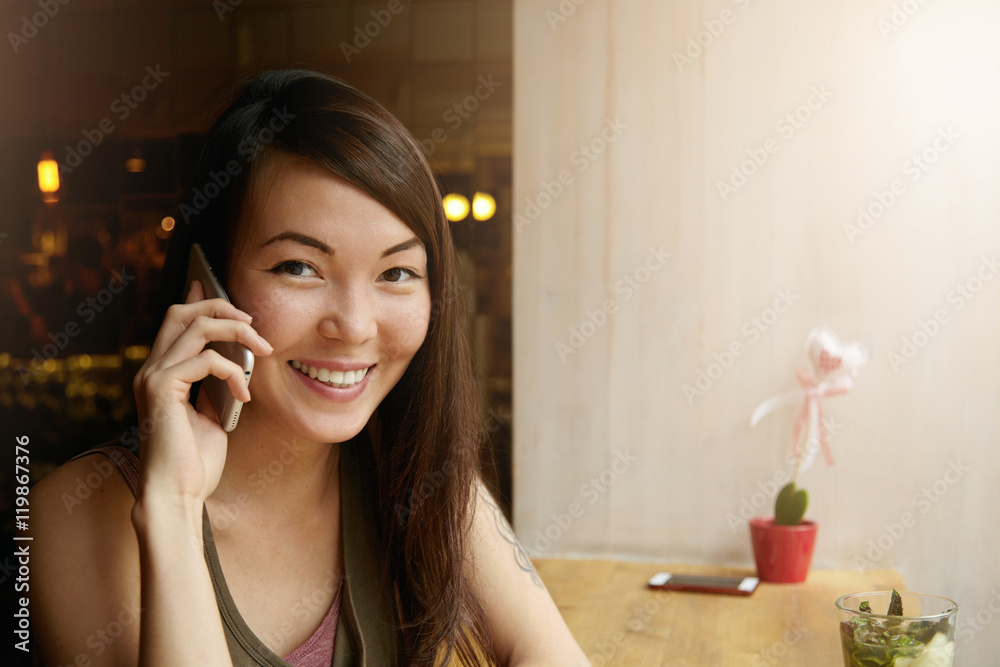 Attractive brunette girl in casual top looking at camera with happy cheerful expression on her face, talking to her best friend, discussing latest news and gossips, having lunch at cozy restaurant Attractive brunette girl in casual top looking at camera with happy cheerful expression on her face, talking to her best friend, discussing latest news and gossips, having lunch at cozy restaurant