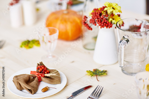 Close up of place setting at autumn dinner table, decorated with pumpkin, maple leaves, rowanberry branches and flowers