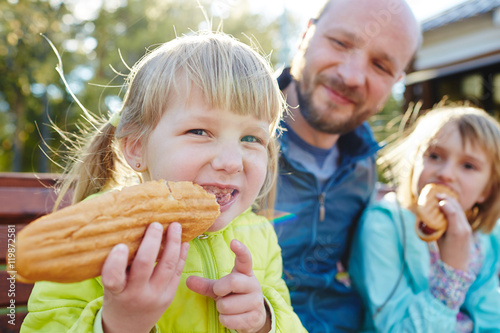 Photography Two blond girls sitting in sunlight on bench with father and enjoying big spicy