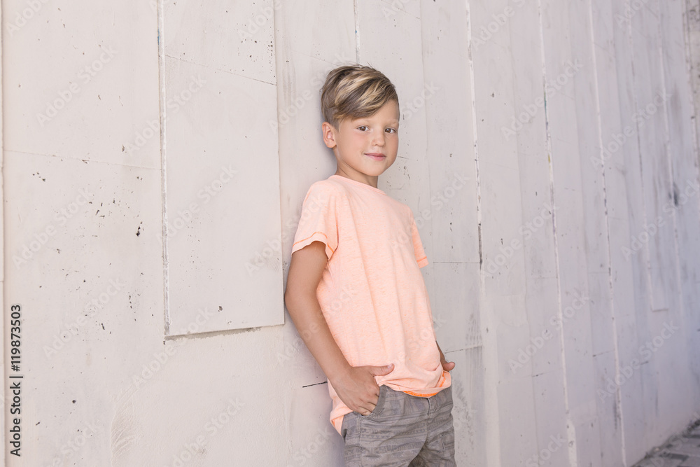 Stylish boy leaned on the wall and looks ahead with a smile . He has cool hair .