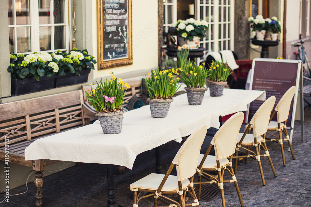 Fototapeta premium Сozy outdoor cafe in Europe with white tablecloth and flower ba