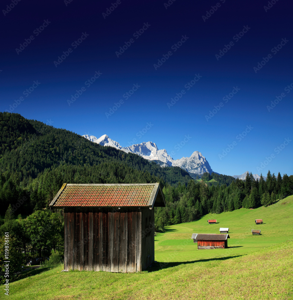 Bergwiese in den Bayerischen Alpen, Typische Almhütten, hinten die Zugspitze, bei Mittenwald, Bayern, Deutschland