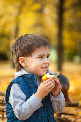 Young boy eating sweet cupcake in autumn park