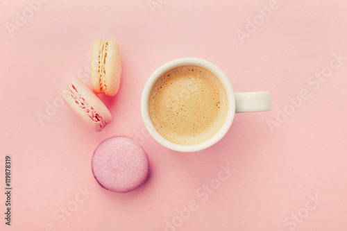 Cup of coffee with macaron on pink background from above, flat lay