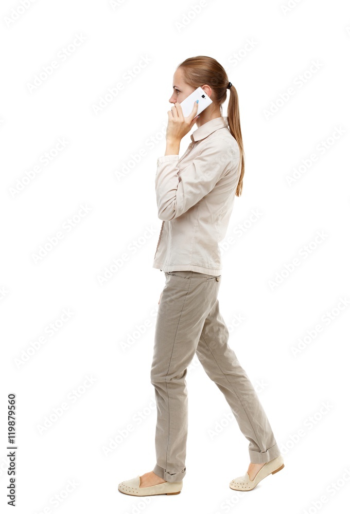 side view of a woman walking with a mobile phone. back view ofgirl in motion. Isolated over white background. Skinny girl in white denim suit talking on the phone while walking. side view of a woman walking with a mobile phone. back view ofgirl in motion. Isolated over white background. Skinny girl in white denim suit talking on the phone while walking.