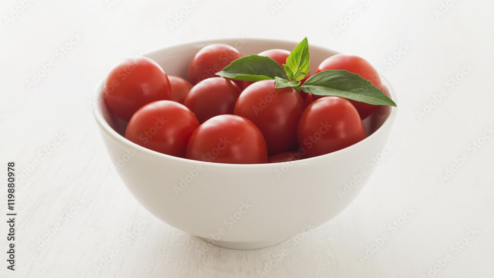 Fresh cherry tomatoes with basil leaves in white bowl Fresh cherry tomatoes with basil leaves in white bowl