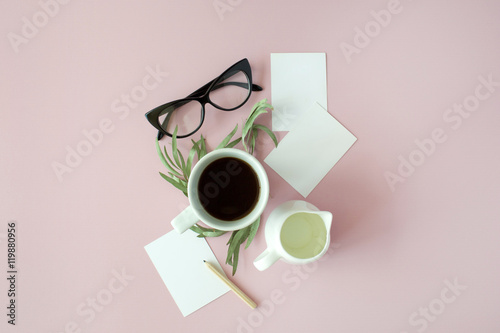 Cup of coffee, paper notes, pencil, green leaves and glasses on pink background. Flat lay, top view