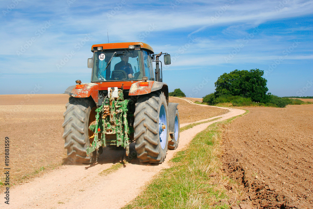 Obraz premium Tractor driving on Dirt Road through Ploughed Fields in Autumn Landscape