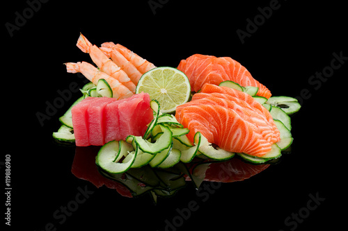 Sashimi set (shrimp, salmon,tuna) with lime and cucumber over black background.