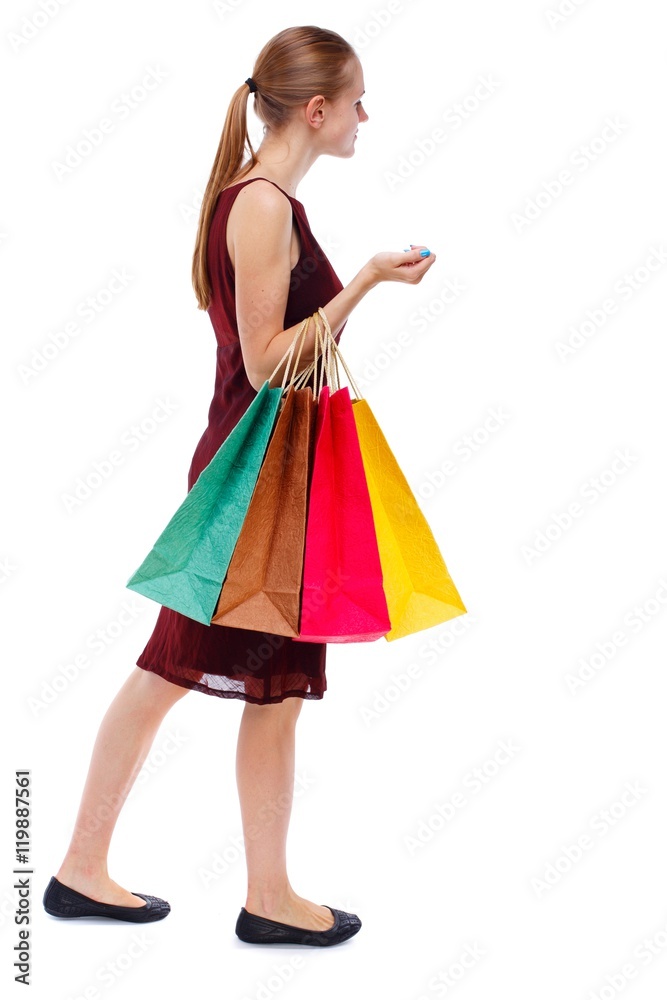 side view of going woman with shopping bags . Isolated over white background. Slim blonde in a burgundy dress shops.