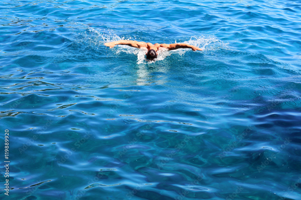 Strong athletic man swimming butterfly style in the sea. Active summer holiday vacation. Sport, healthy lifestyle concept