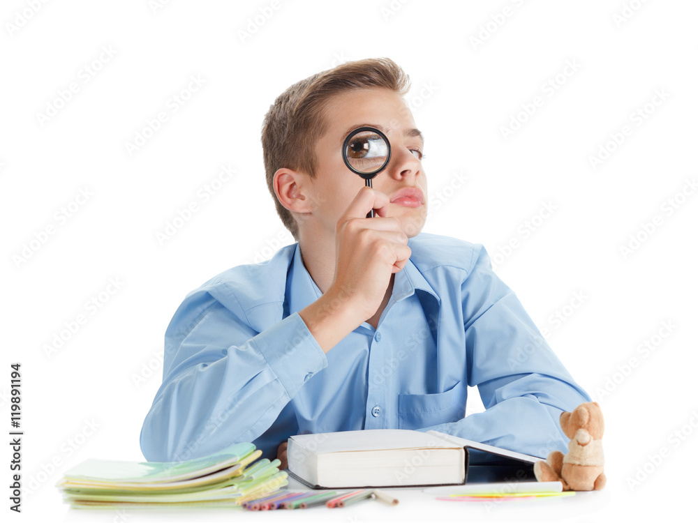 Fun schoolboy sits near the desk with school supplies isolated on white. Fun schoolboy sits near the desk with school supplies isolated on white.