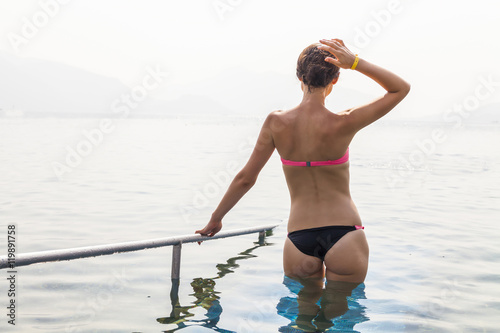 Slim tanned young woman in the sea. View from the back.