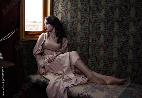 Картината върху платно Young woman in beige vintage dress of early 20th century sitting