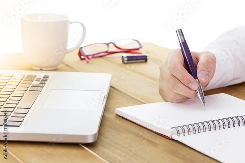 Businessman write a short note on opened notebook with pen and glasses. warm tone.