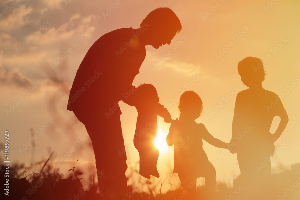 silhouette of happy father with tree kids at sunset sky