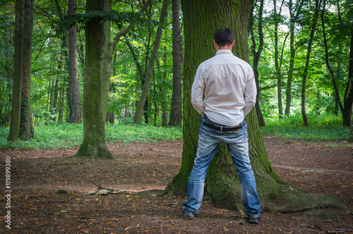 Obraz na płótnie Standing man peeing near big tree in summer forest