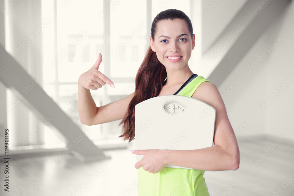 Young beautiful woman with bottle and scales on blurred hall background.