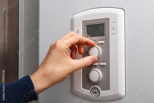 Men hand regulate temperature on 55 degree in control panel of central heating.