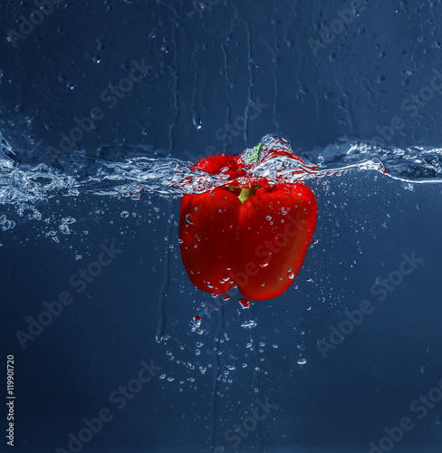 Fresh red bell pepper falling in water on dark background