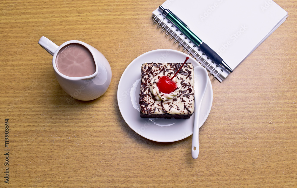 Chocolate cake with cherry and milk jug, notebook, cactus on woo