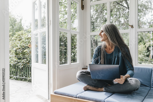 Woman with laptop sitting on lounge in winter garden looking through opened terrace door