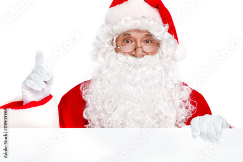 Traditional Santa Claus pointing up and holding white banner on white background. Copy space © dream_stock