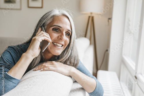 Smiling woman sitting on the couch telephoning with cell phone