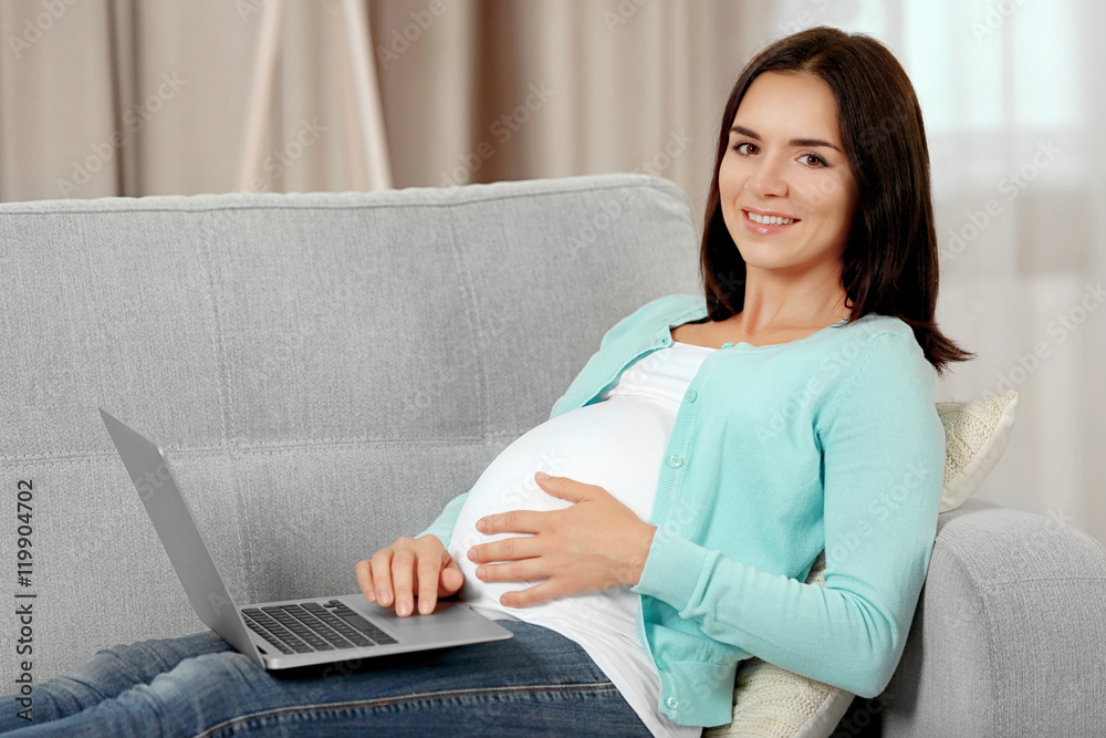 Pregnant woman with laptop sitting on sofa in the room Pregnant woman with laptop sitting on sofa in the room