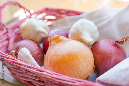 Fototapeta Naklejka Na Ścianę i Meble -  Ingredienti per cucinare: cipolle e aglio in una cesta rosa