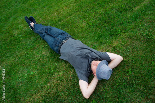 man lying in a field on green grass with the hat over his face