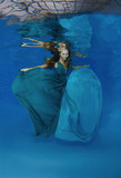 Young beautiful woman with long hair in a bright green-blue dress under water, underwater fashion in the pool, Odessa, Ukraine