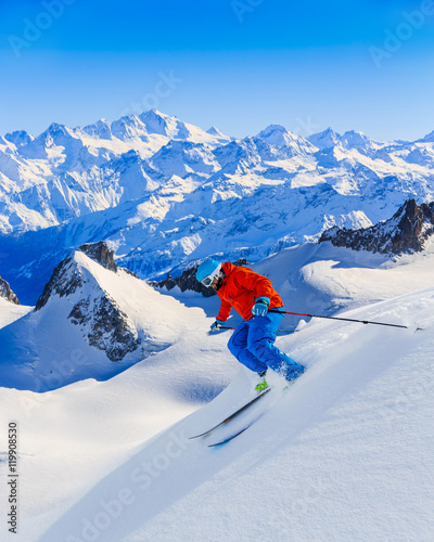 Male skier skiing in fresh snow off ski slope on a sunny winter day at high mountain in French Alps. Freeski in powder snow.