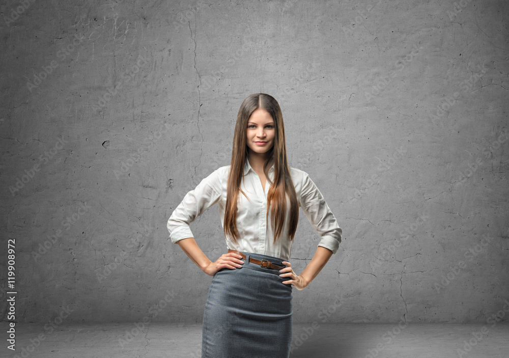 Young businesswoman holding her hands on waist in the background of concrete wall Young businesswoman holding her hands on waist in the background of concrete wall