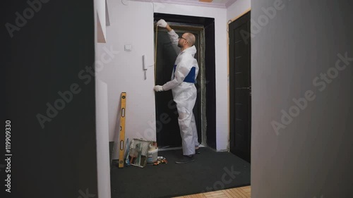 Worker in overalls, takes measurements of the doorway, he was a professional builder. The man with glasses is preparing to make repairs or replace the door. photo